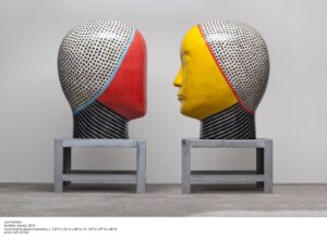 A photo of 2 large head sculptures. The heads face each other and stand about 10 feel tall each.