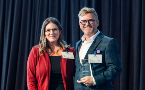 Craig Wilson, JD, receives the HWHI Bridge Award on stage from Sarah Bemis, DNP.