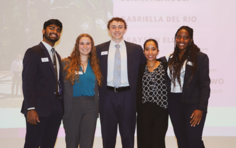 5 Morehead-Cain Scholars stand on stage and pose for a group photo following their presentation.
