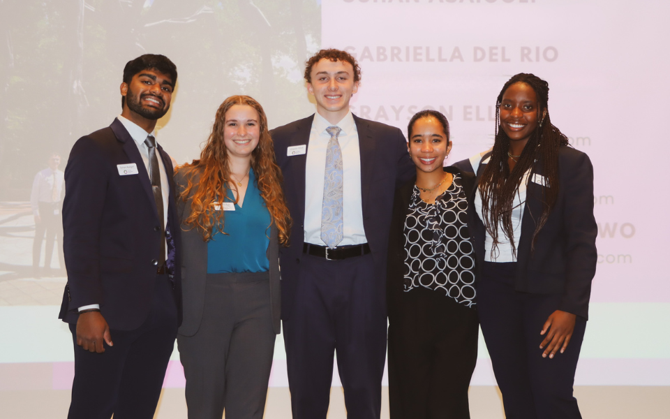 5 Morehead-Cain Scholars stand on stage and pose for a group photo following their presentation.
